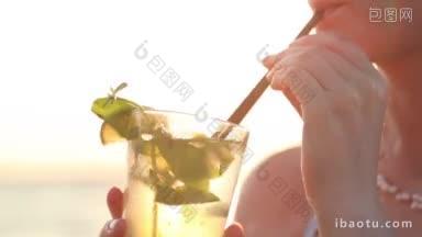 特写的女人享受莫吉托鸡尾酒在海边在日落通过<strong>吸管</strong>喝它